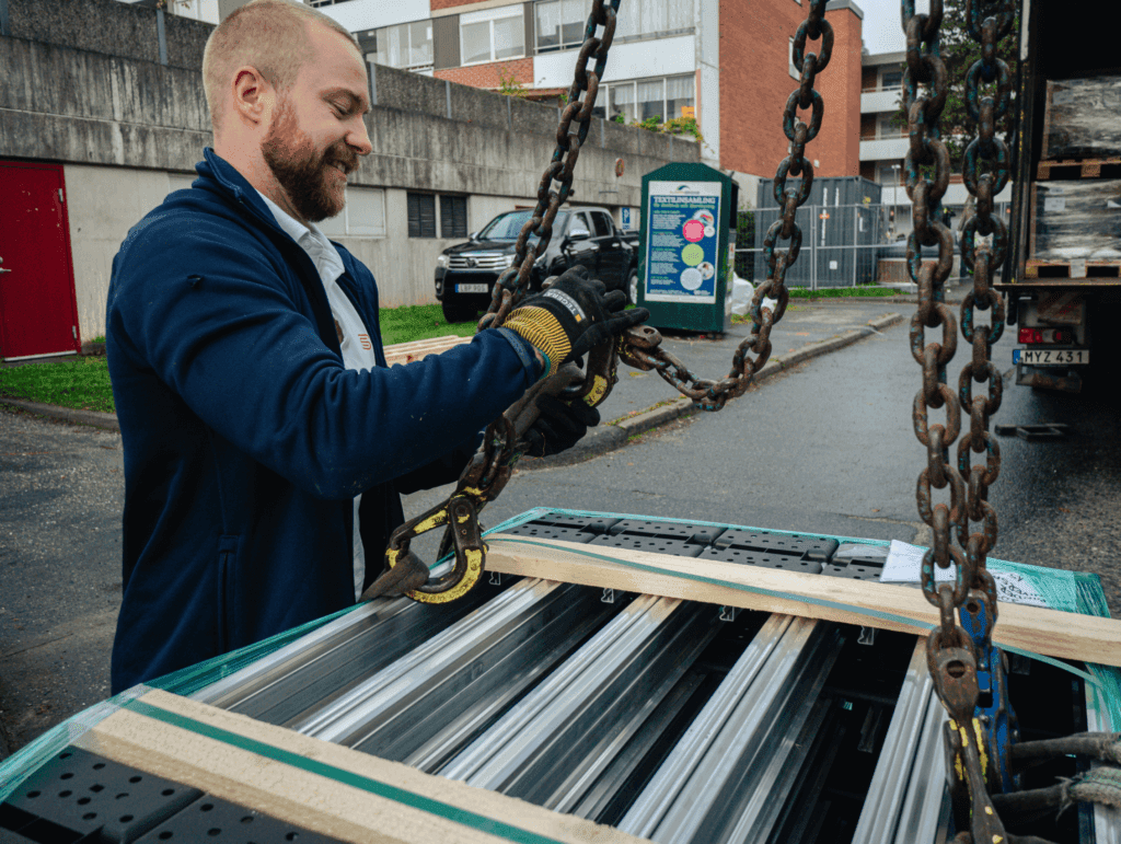 Stockholms Elpartner tar emot en leverans från leverantör. Glad medarbetare tar emot en lastad pall utanför lastbil i bostadsområde.